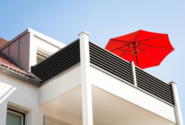 Ansicht aus der Froschperspektive auf ein Balkongeländer mit Sichtschutz und einem roten Sonnenschirm