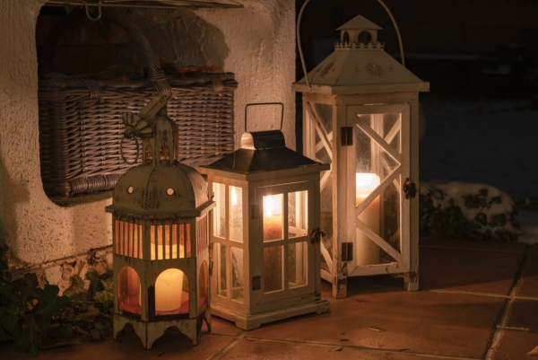 Drei Laternen aus Holz mit Kerzen darin stehen auf einer Steinplatte an der Hauswand